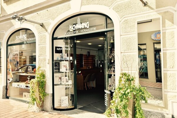 Fassade eines Optiker- und Hörakustikgeschäfts mit Schaufenster und Pflanzen am Eingang.